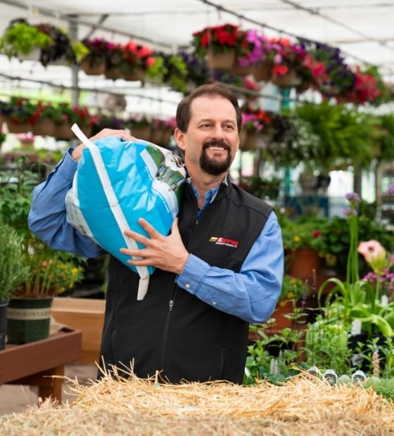 Man carrying a bag of soil in a greenhouse