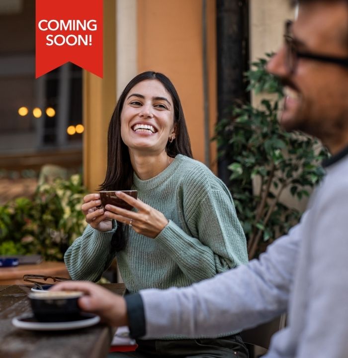 Coming soon! Women and man sitting at an outdoor cafe smiling